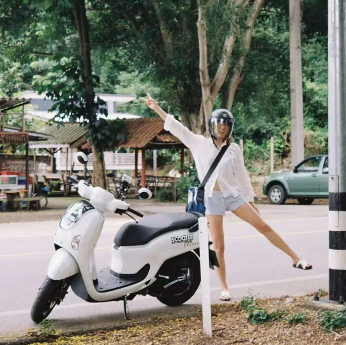 a girl posing in front of a scooter hub scooter in the forest